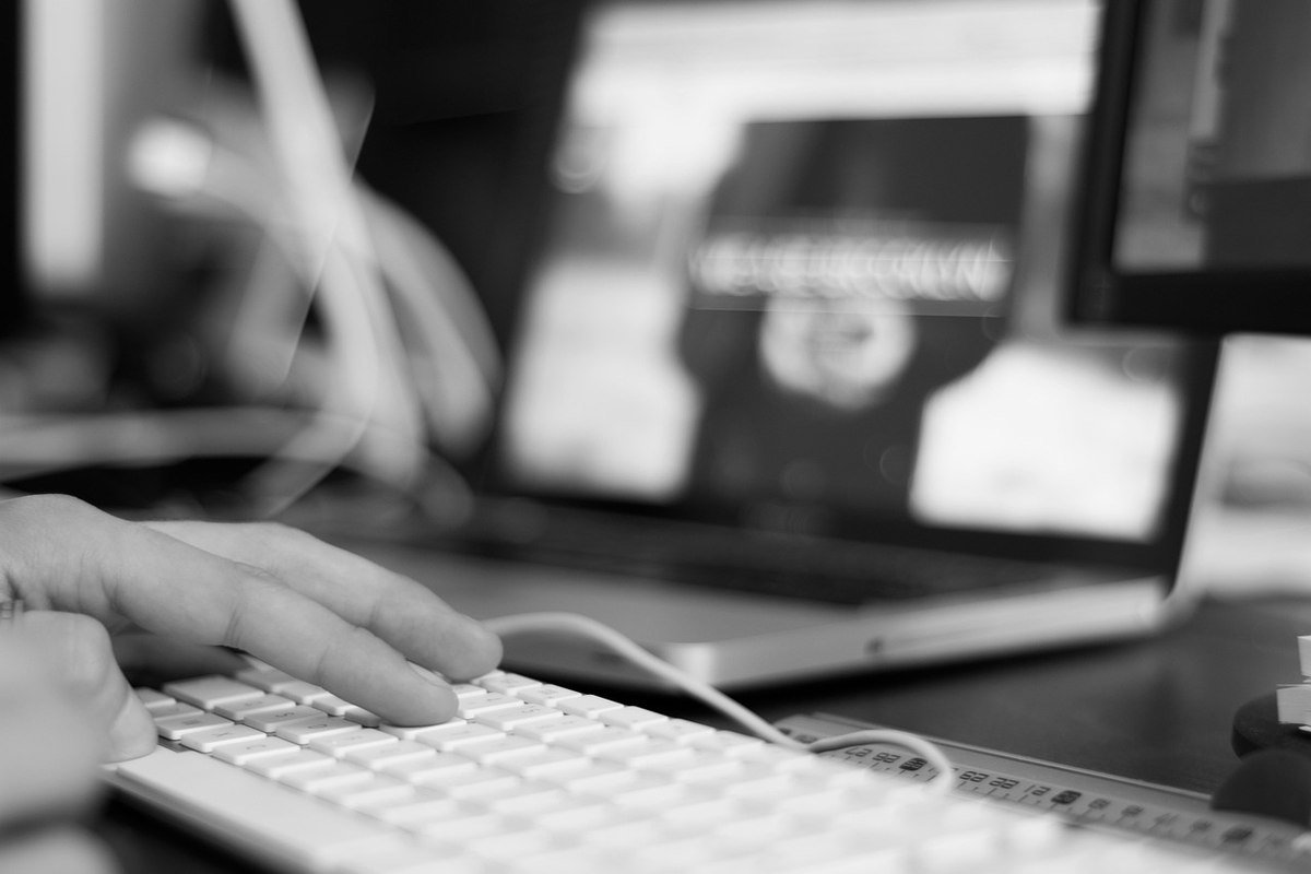 Main d'une personne tapant sur un clavier d'ordinateur, avec un écran d'ordinateur portable flou en arrière-plan