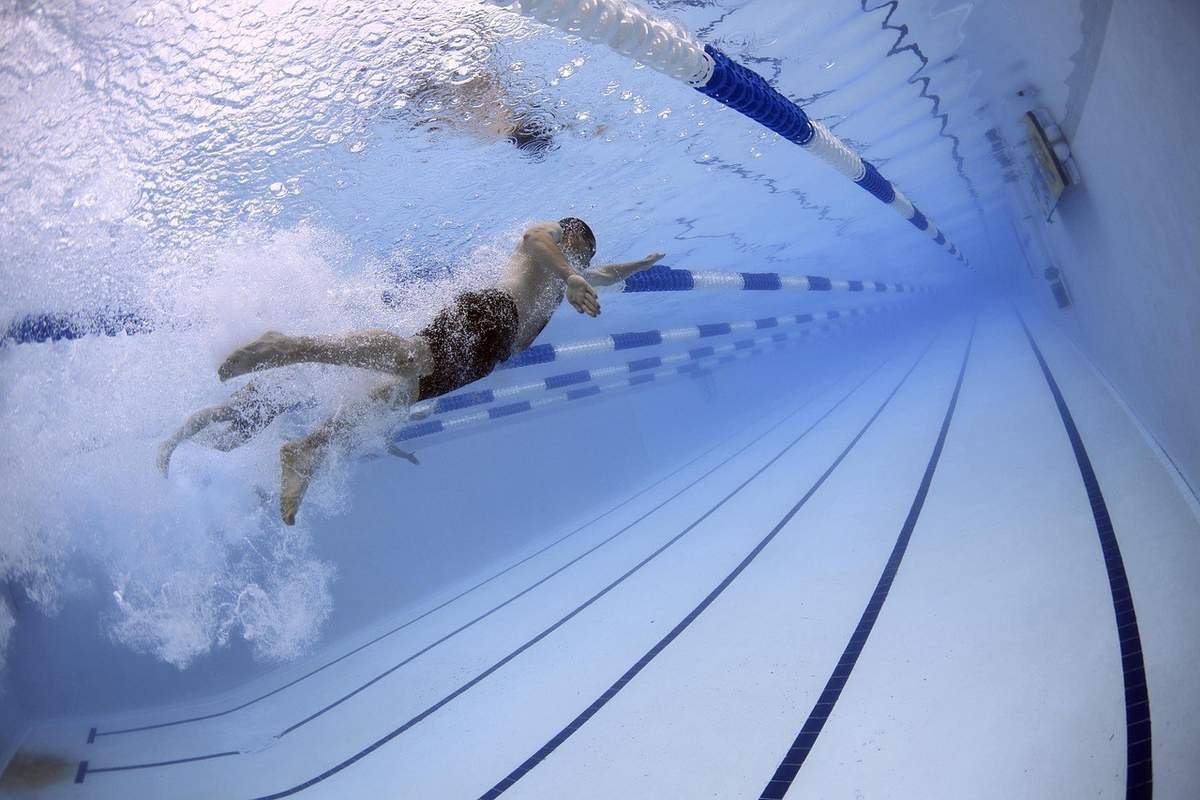 Nageur en action dans une piscine, bras écartés, eau trouble, lignes de la piscine visibles
