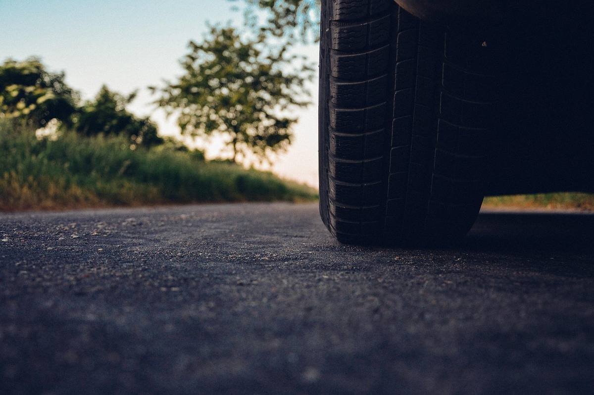 Pneu de voiture sur route, bordée d'herbe et d'arbres, au crépuscule Pneu de voiture sur route, bordée d'herbe et d'arbres, au crépuscule