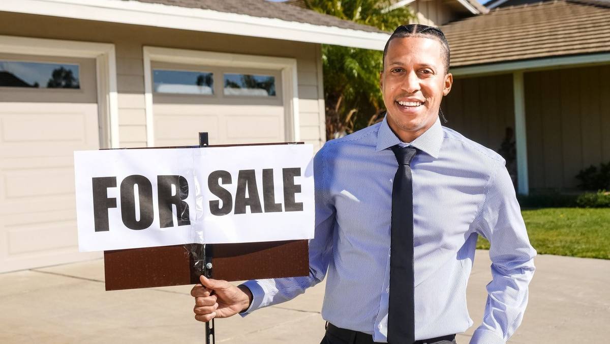 Homme souriant devant maison avec panneau 